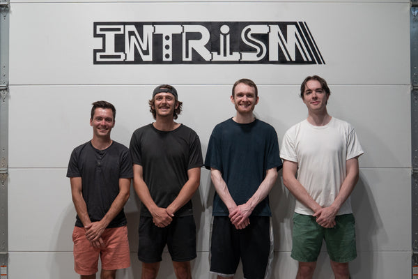 Four men standing in front of a white wall with 'INTRISM' branding.